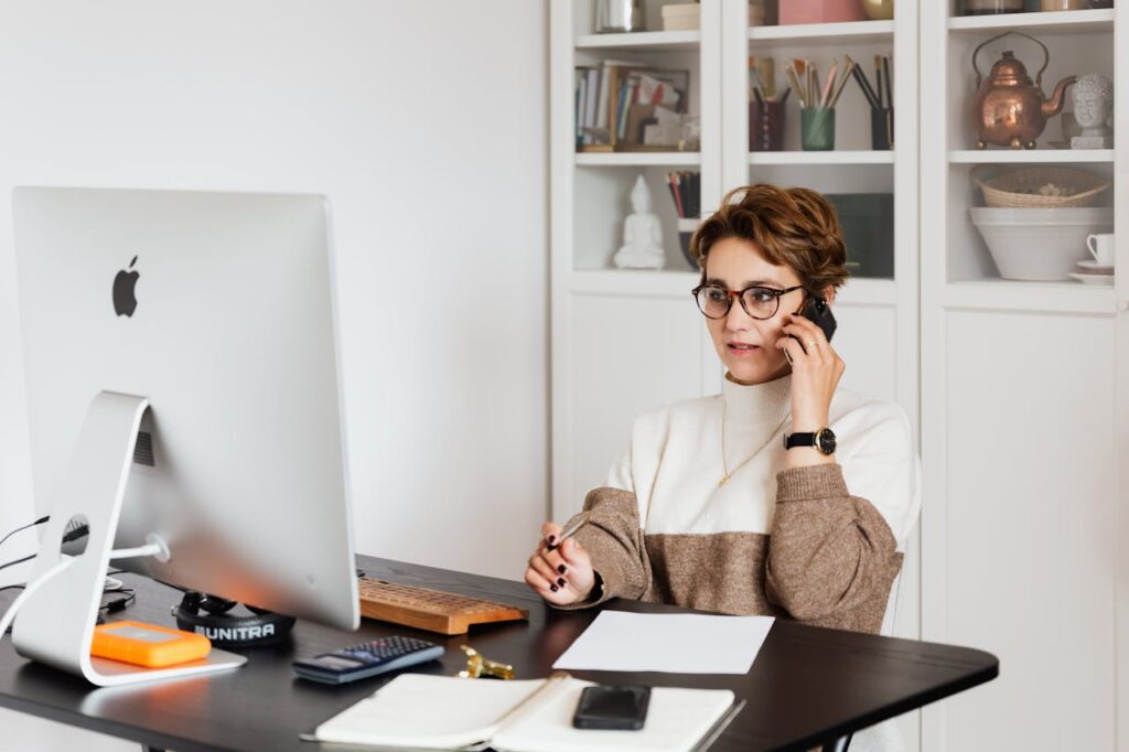 Une gestionnaire de copropriété professionnelle au travail, consultant des documents comptables et parlant au téléphone devant un ordinateur.