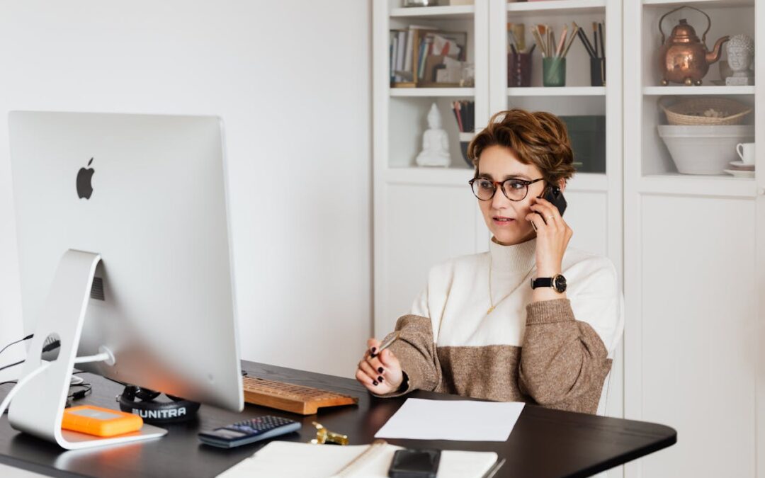 Une gestionnaire de copropriété professionnelle au travail, consultant des documents comptables et parlant au téléphone devant un ordinateur.